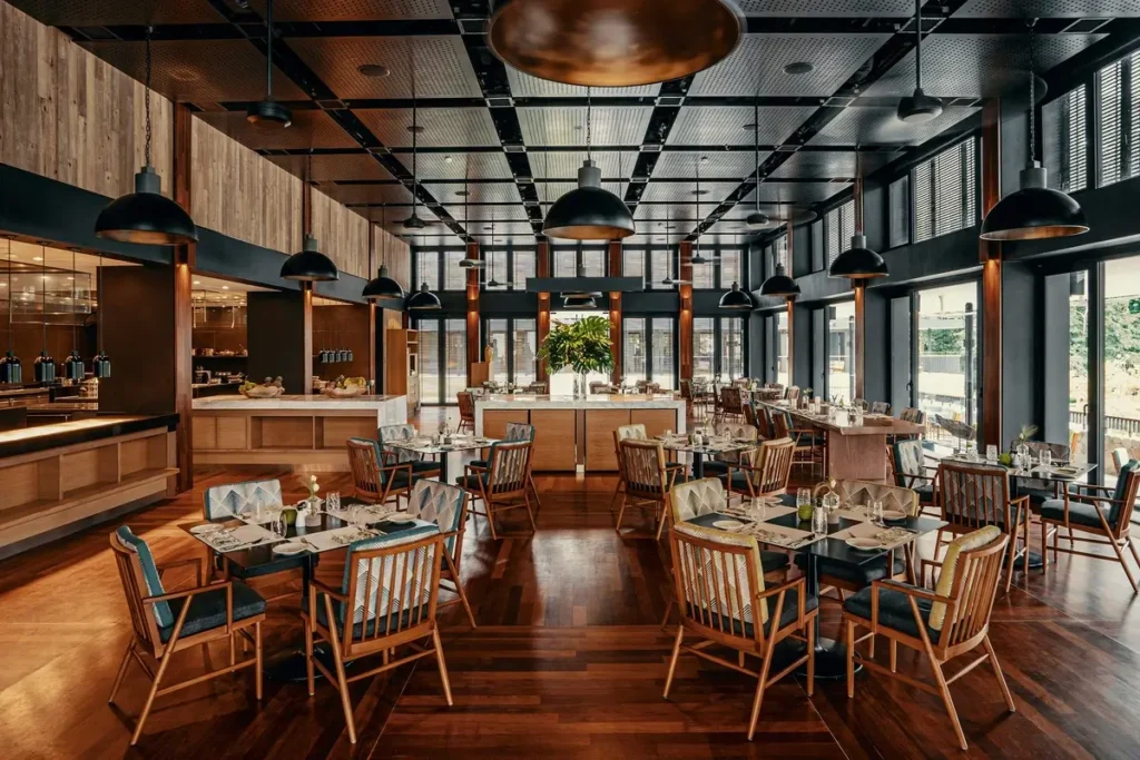 Wooden tables, patterned chairs, pendant lights, and tall windows inside Ambara restaurant.
