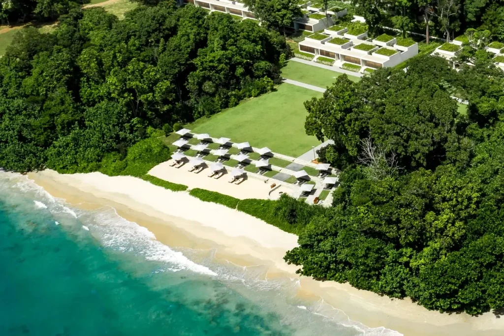 Aerial view of Ocean Lawn, beachfront suites, and a sandy stretch of shoreline surrounded by trees.