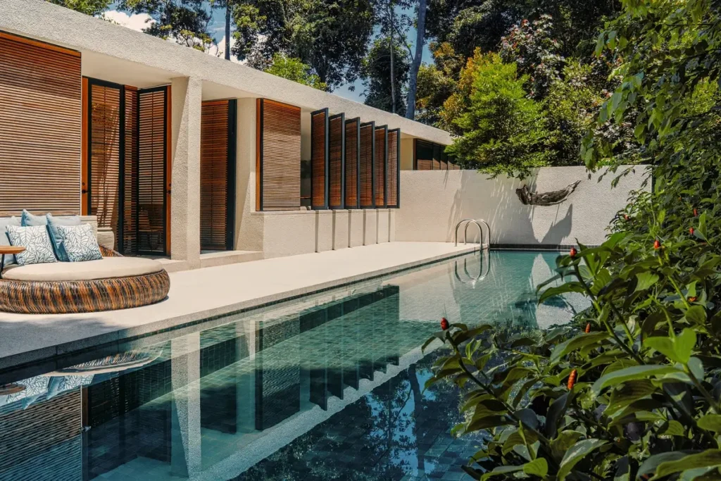 Long private pool beside a terrace and glass-fronted suite, with trees and shrubs around the water.
