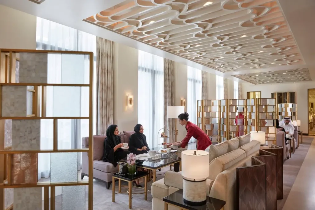 Light-colored sofas, small tables, decorative ceiling panels, and tall windows in Baraha Lounge.