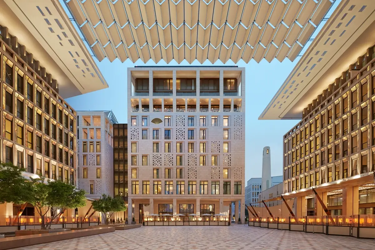 Mandarin Oriental, Doha overlooking a paved square framed by pale stone buildings and an overhead shade structure.