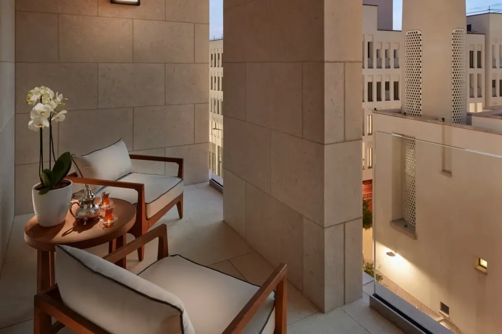 Chairs and a small table on a sheltered Junior Suite balcony looking toward neighboring Msheireb buildings.