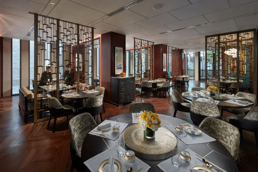 Set dining tables, upholstered chairs, dark wood screens, and tall windows in Liang at Mandarin Oriental, Doha.
