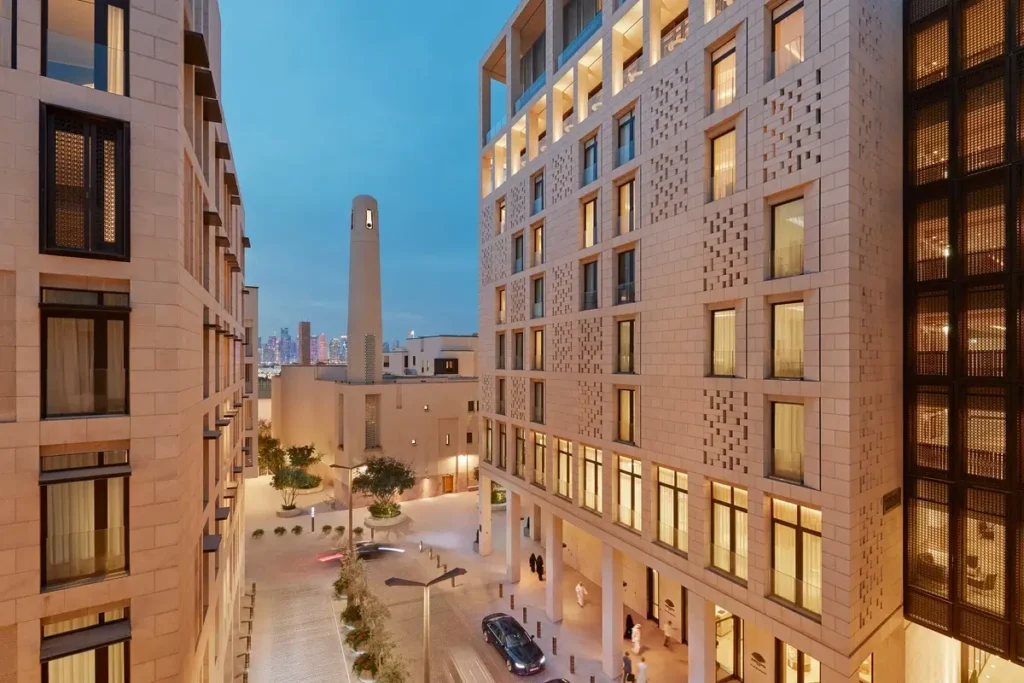 Pale stone hotel facades, trees, and cars along a street beside Mandarin Oriental, Doha.