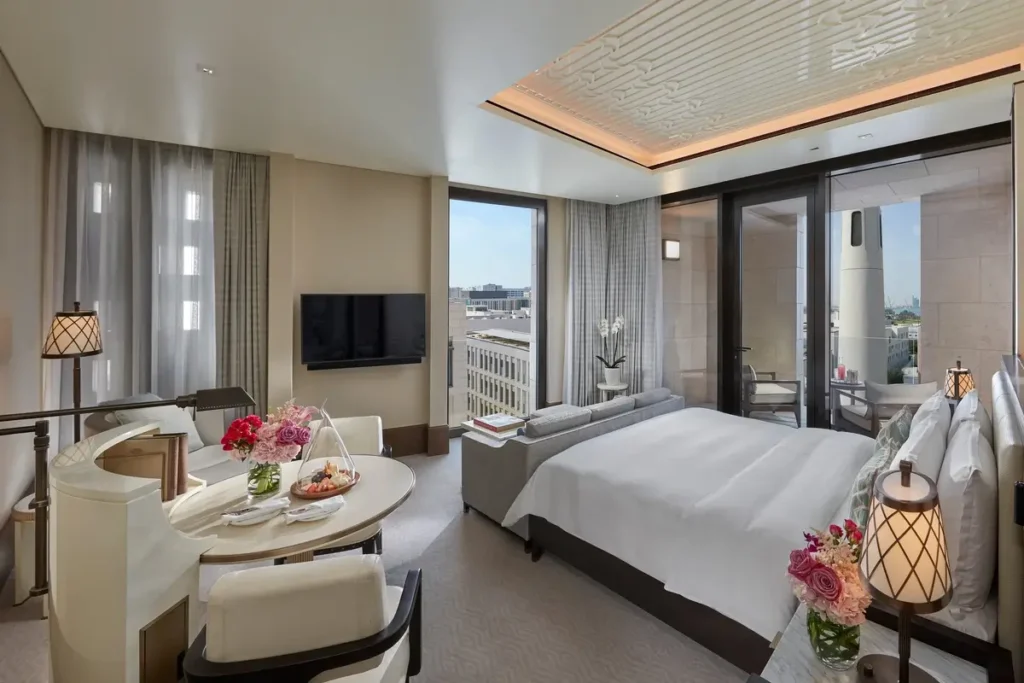 Bed, curved sofa, dining table, and tall windows in a Premier Room at Mandarin Oriental, Doha.