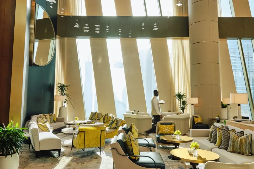 Cream sofas, yellow armchairs, low tables, plants, and tall sloping windows in The Lobby Lounge.
