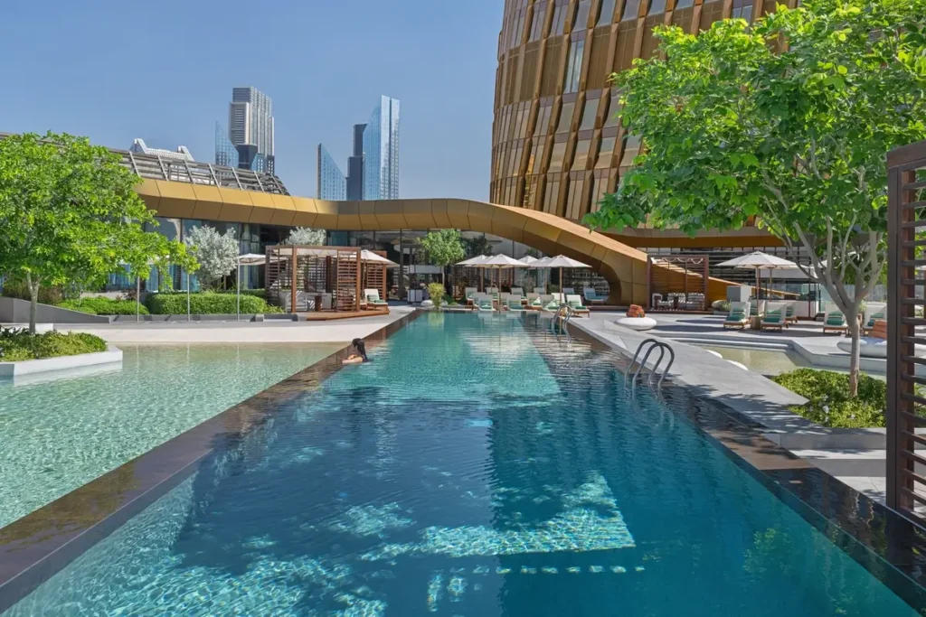 Long outdoor swimming pool with lane markings, loungers, trees, and shade structures at Mandarin Oriental Downtown.