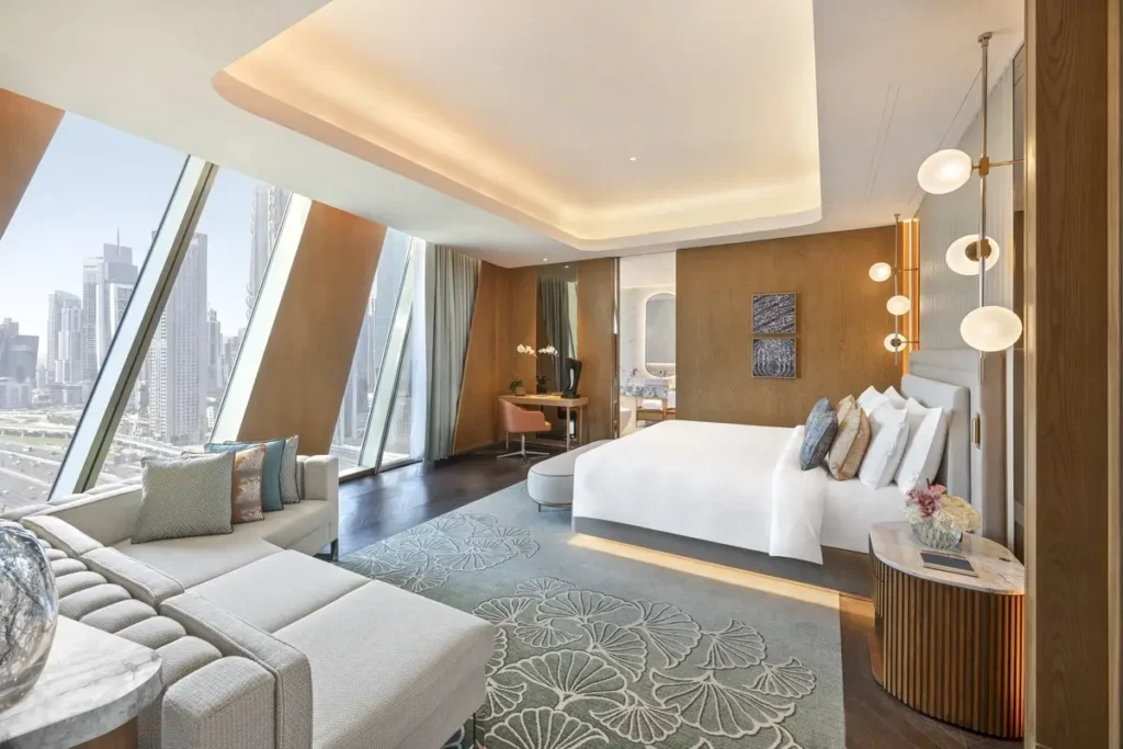 Bed, sofa, dining table, and sloping floor-to-ceiling windows overlooking Dubai in a Premier Downtown View Room.