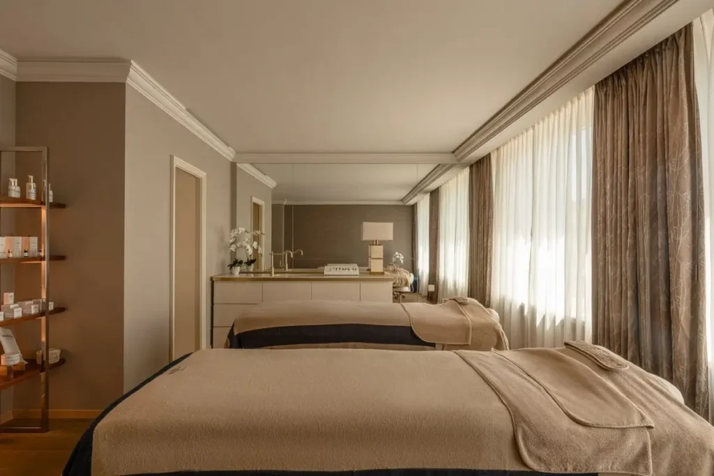 Treatment bed, skincare display, mirrors, and tall curtained windows in a Biologique Recherche beauty suite.