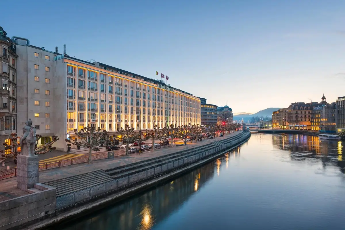 Illuminated facade of Mandarin Oriental, Geneva beside the Rhône at dusk.