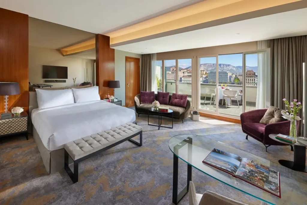 Bedroom and sitting area with burgundy chairs and windows opening toward the terrace in a Junior Terrace Suite.