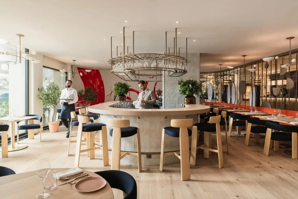 Light-filled Ottolenghi dining room with a central counter, wood tables, and pendant lights.