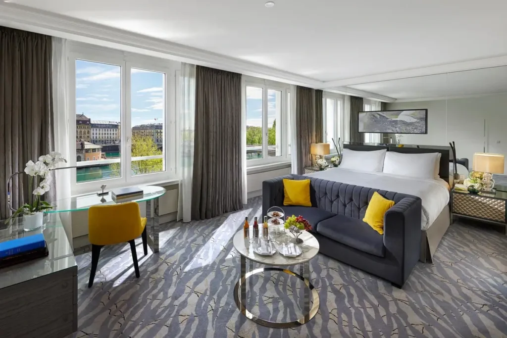 Bed, gray sofa with yellow cushions, glass tables, and river-facing windows in a River View Mandarin Room.