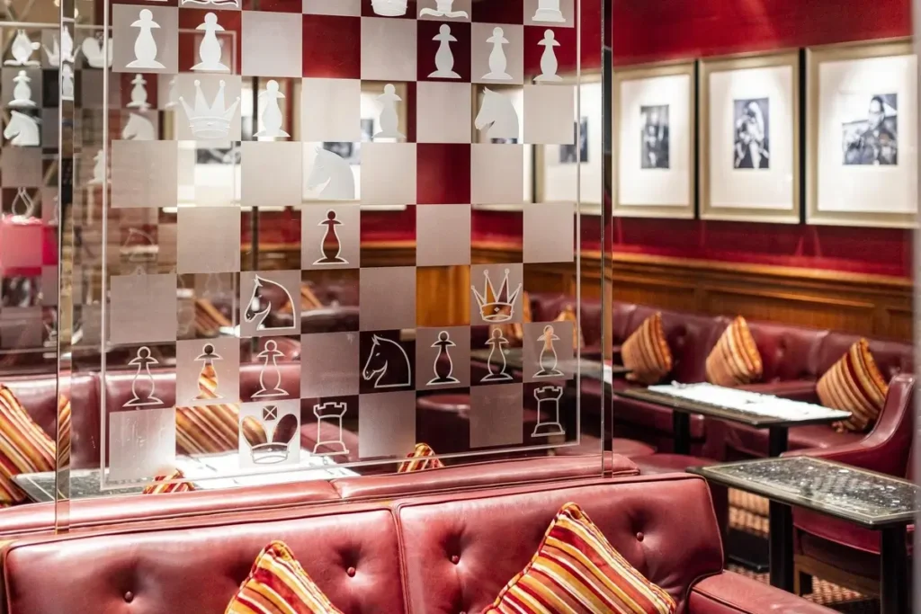 Red leather seating, dark wood tables, framed pictures, and a decorative display at Captain’s Bar.