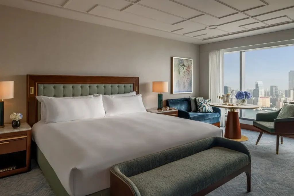 King bed, upholstered bench, armchairs, and a broad window overlooking Victoria Harbour in a Harbour View Room.
