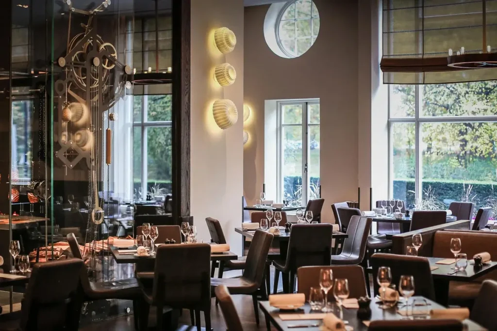 Set dining tables, upholstered chairs, and broad windows overlooking greenery at Dinner by Heston Blumenthal.