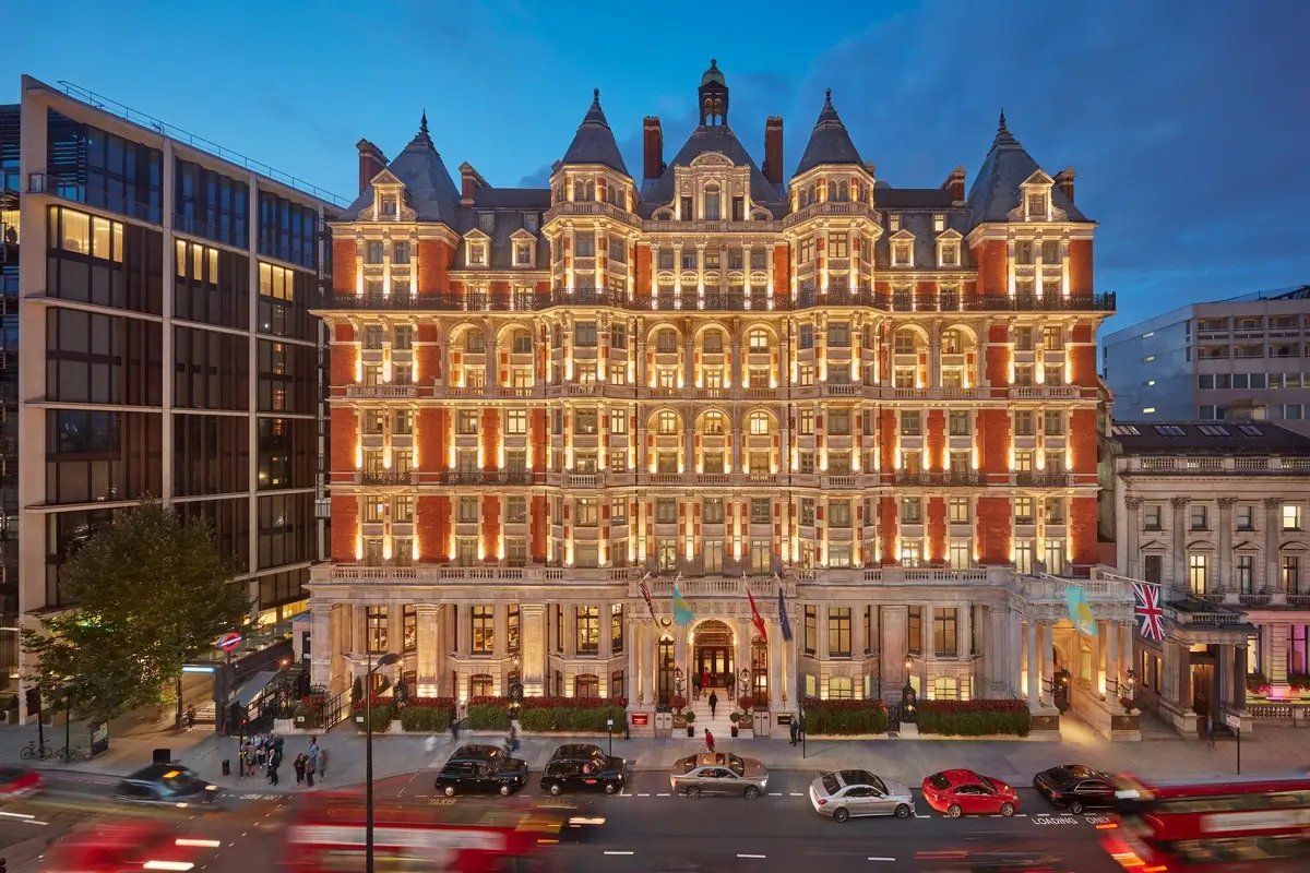 Illuminated red-brick facade of Mandarin Oriental Hyde Park above Knightsbridge traffic at dusk.