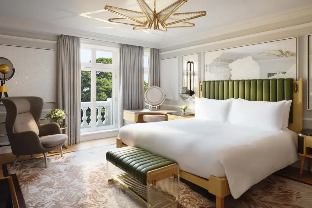 Bed with a green headboard, matching bench, armchair, and windows toward greenery in a Hyde Park Suite bedroom.