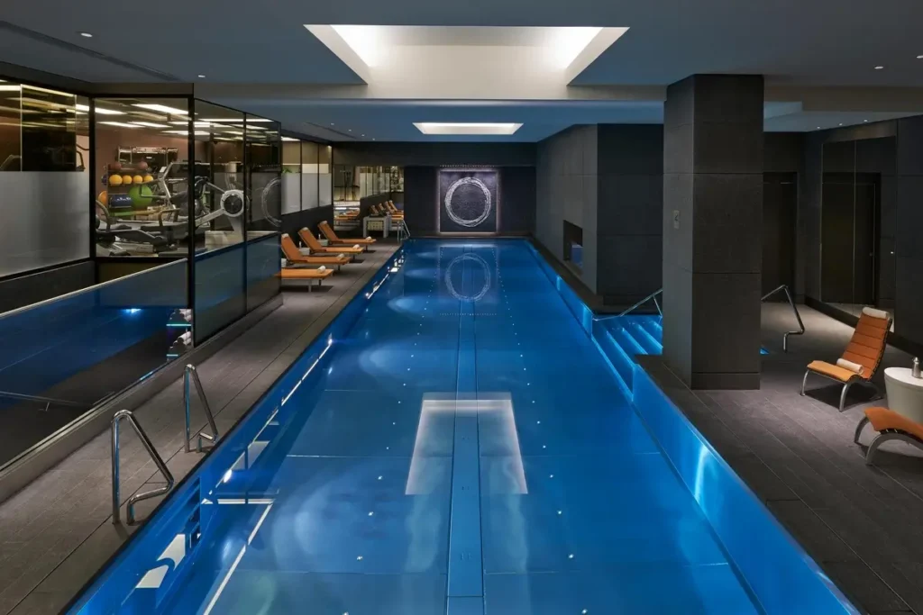 Long indoor swimming pool with lane markings, dark columns, and loungers along one side.