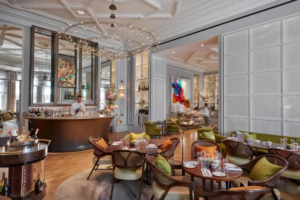 Tables, colorful upholstered chairs, decorative lighting, and tall windows in The Rosebery.