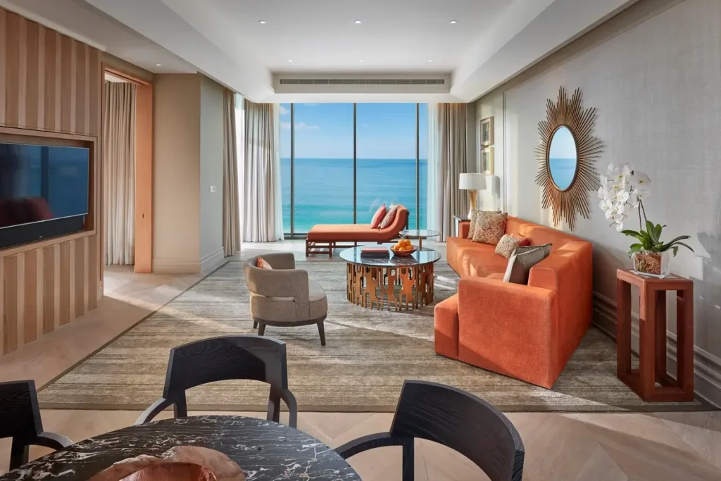 Orange sofa, armchairs, dining space, and tall windows overlooking the sea in the Mandarin Sea Front Suite.