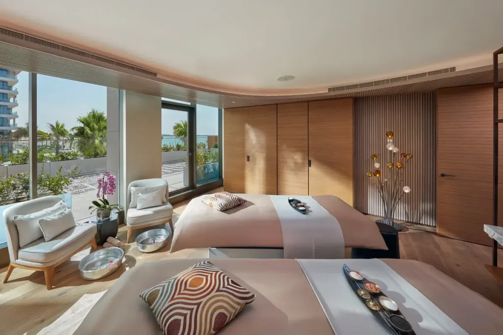 Two treatment beds, seating, timber wall panels, and broad windows in the VIP Spa Suite.