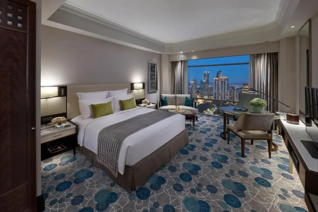King bed, seating, desk, and windows overlooking the park and illuminated city buildings in a Deluxe Park View Room.