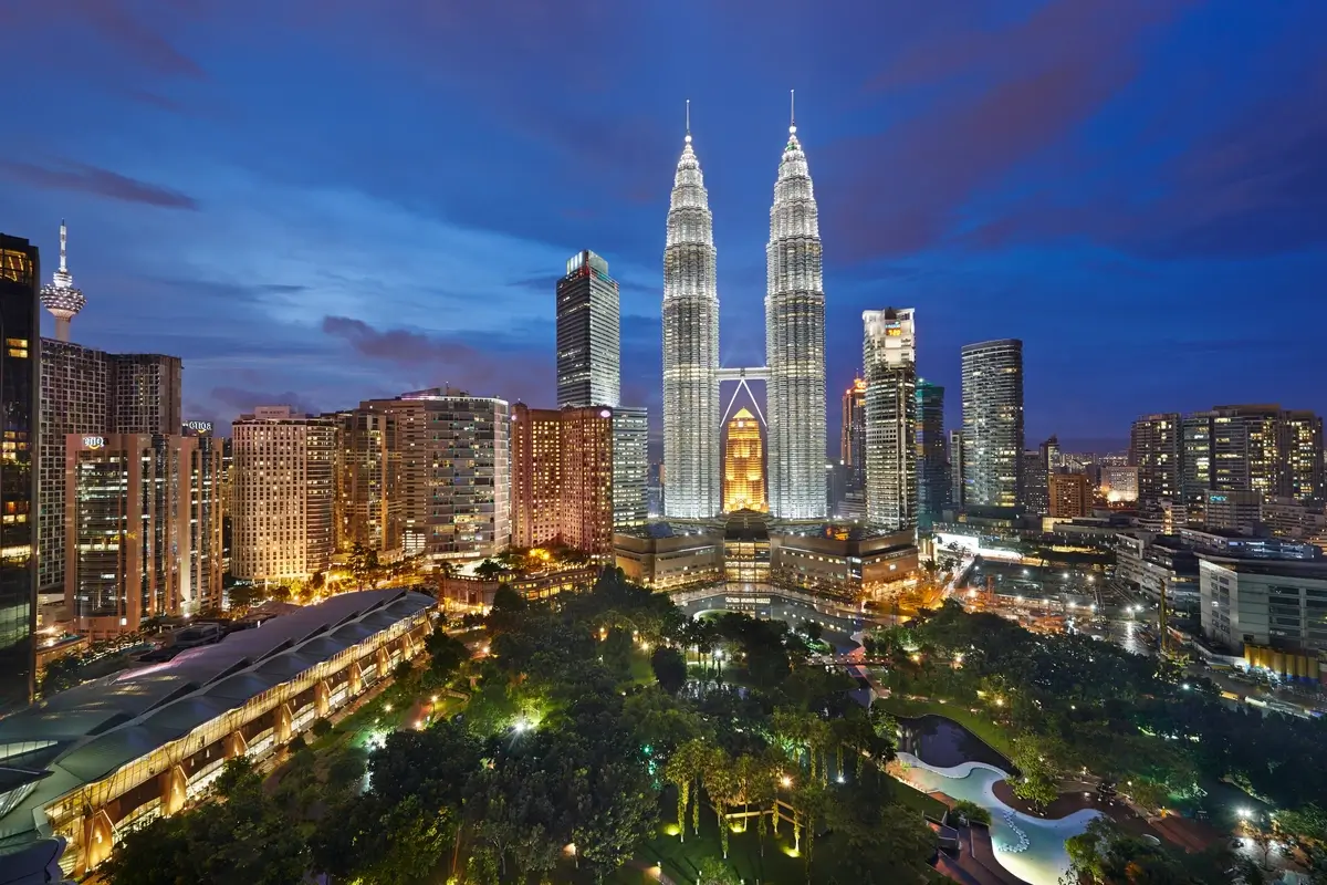 Petronas Twin Towers and surrounding buildings above the landscaped park at dusk.