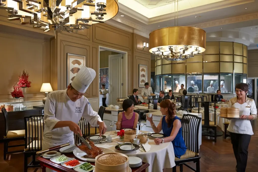 Chef serving guests at a dining table beneath gold-toned chandeliers in Lai Po Heen.