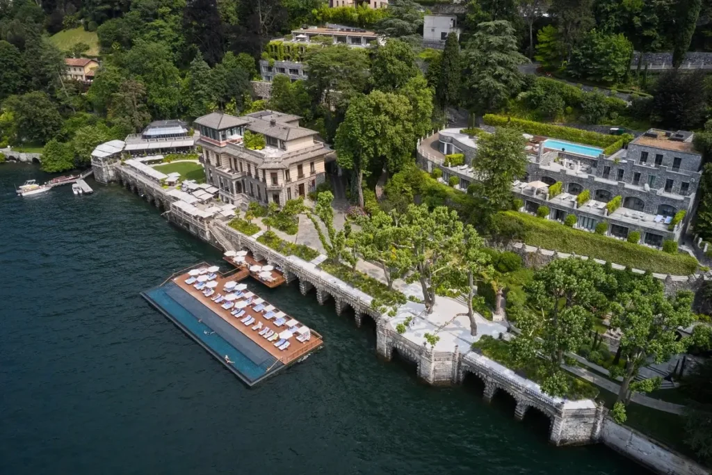 Aerial view of the floating pool platform and loungers beside the resort’s waterfront buildings.