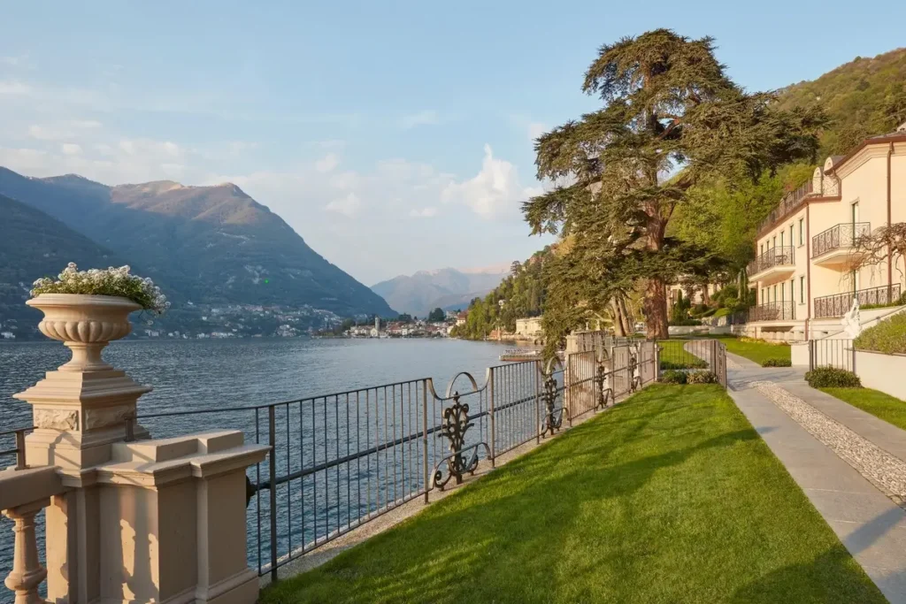 Lawn, stone balustrade, pathway, and resort buildings beside Lake Como, with mountains across the water.
