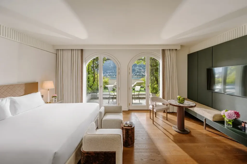 Bed, seating, wood floors, and arched glass doors facing a lake-view balcony in a Vista Lago Room.