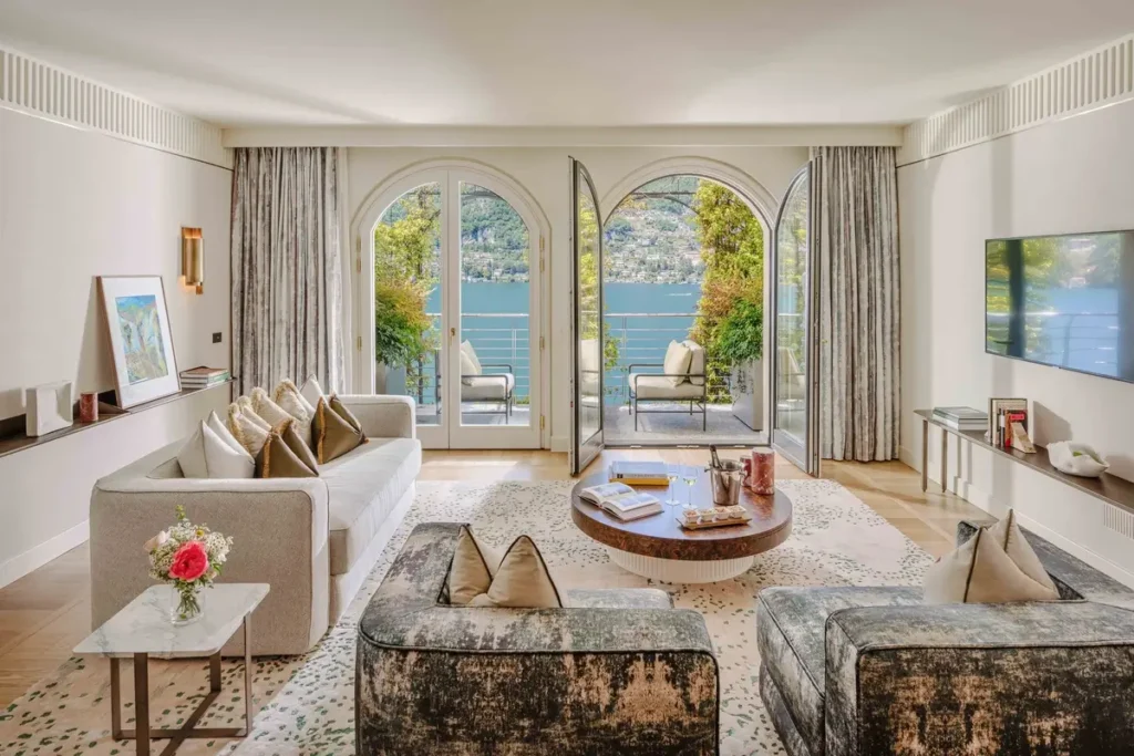 Sofa, armchairs, coffee table, and arched glass doors opening toward Lake Como in a Vista Lago Suite.