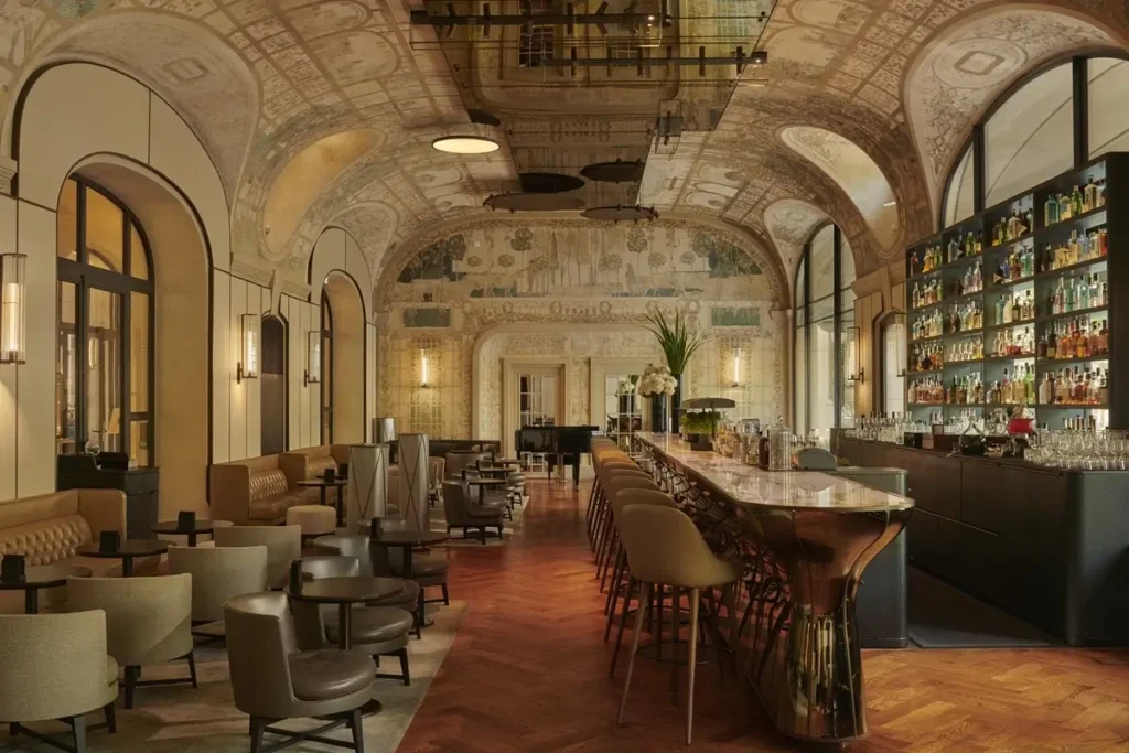 Long bar, upholstered seating, arched windows, and ornate painted ceilings in Bar Joséphine.