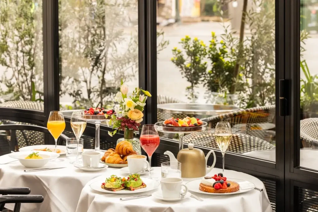 Breakfast dishes, pastries, juice, and coffee arranged on a white-clothed table beside tall windows at Brasserie Lutetia.
