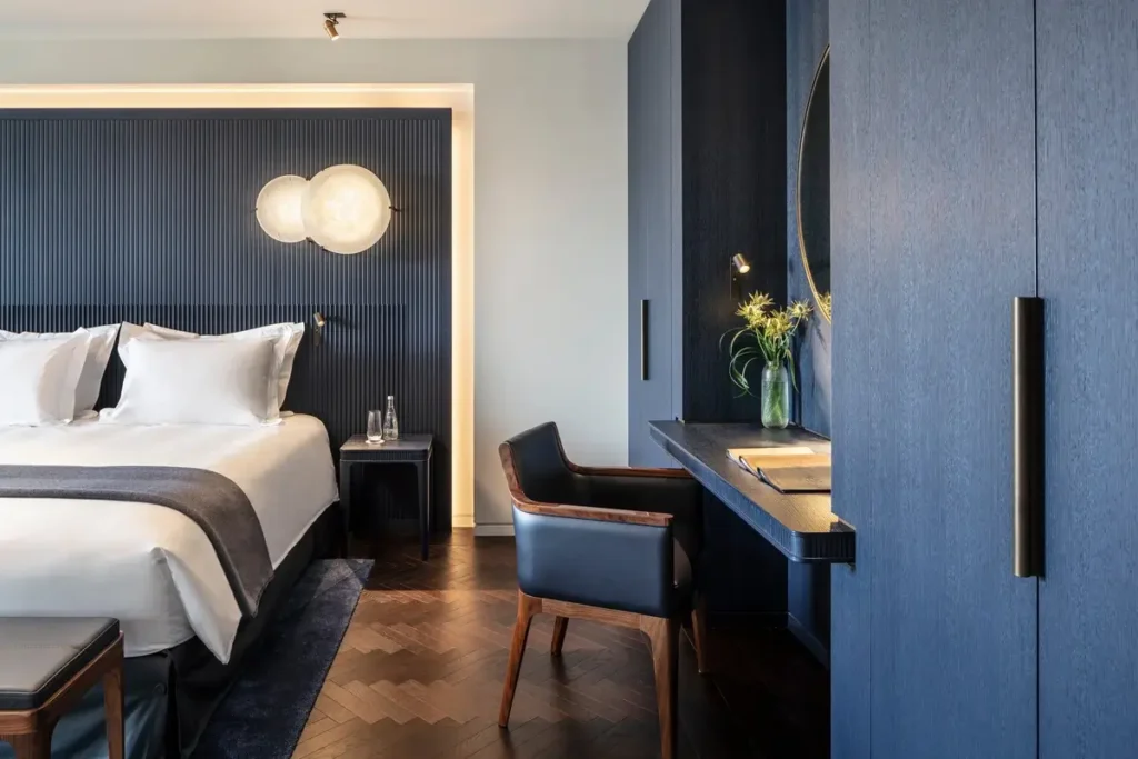 Bed, armchair, desk, and dark blue paneling in an Eiffel-view deluxe balcony room at Lutetia.