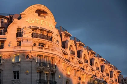 Illuminated curved stone facade of Mandarin Oriental Lutetia, Paris, with carved details and balconies beneath a dark sky.