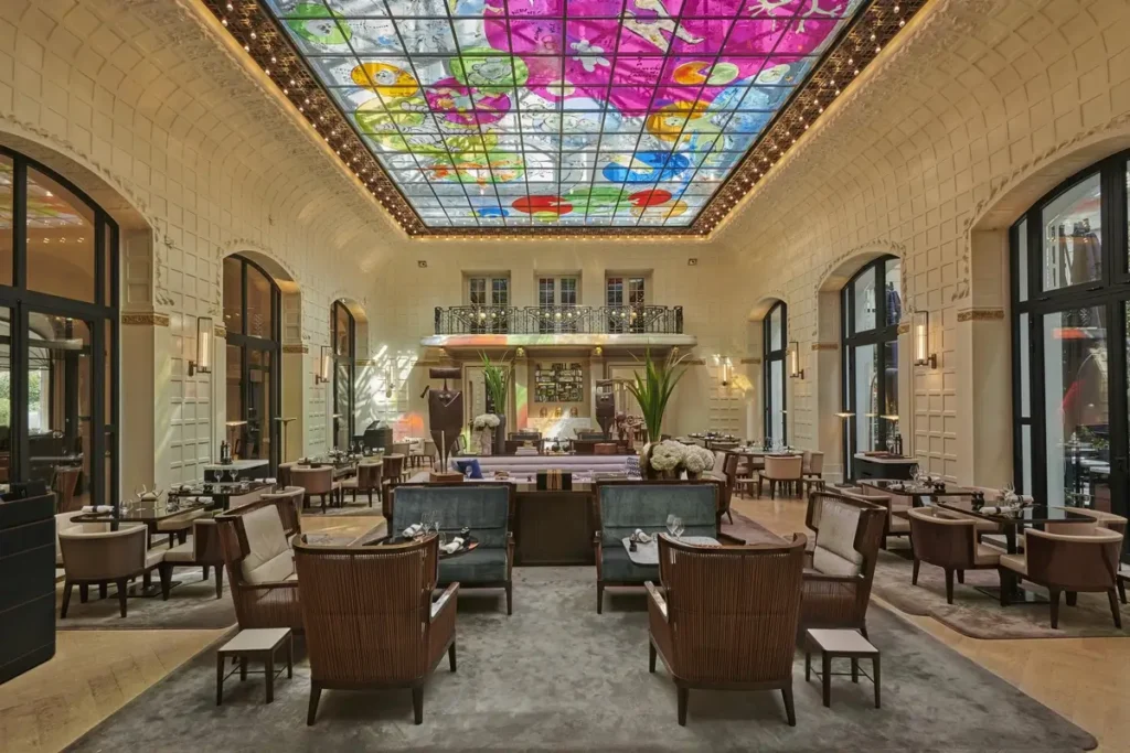 Armchairs and tables beneath a colorful painted-glass ceiling in Le Saint-Germain at Lutetia.