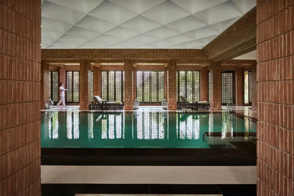 Indoor swimming pool framed by stone walls and columns, with loungers and windows beyond.