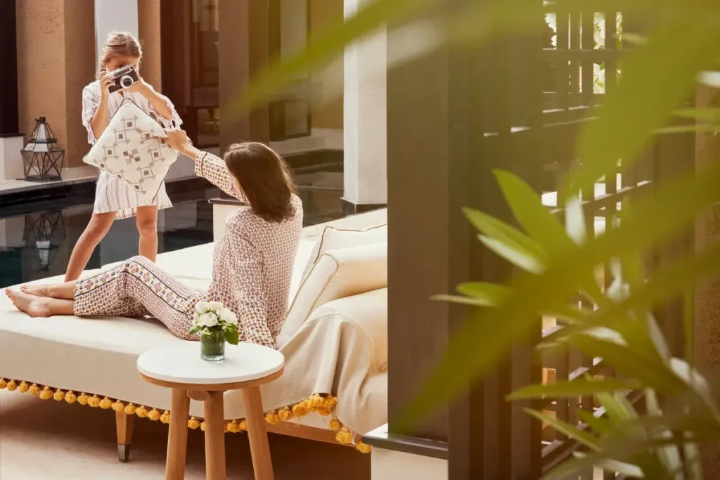 Adult and child beside a cushioned daybed in a shaded Mandarin Pool Villa outdoor sitting area.