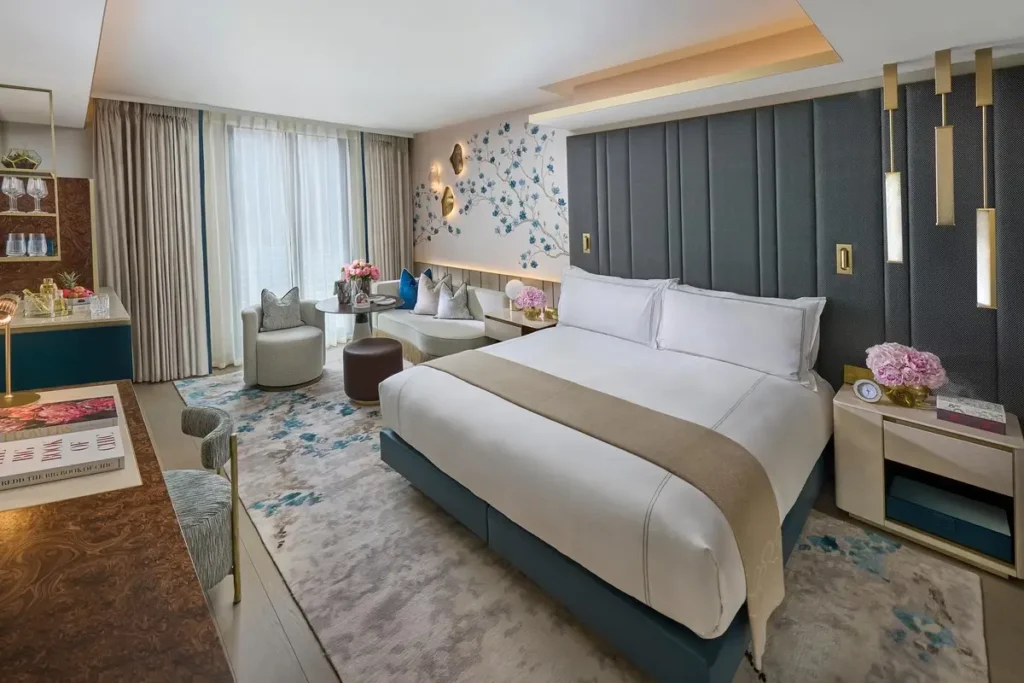 Bed, floral wallpaper, patterned carpet, and a small sitting area in a Deluxe Room at Mandarin Oriental Mayfair.