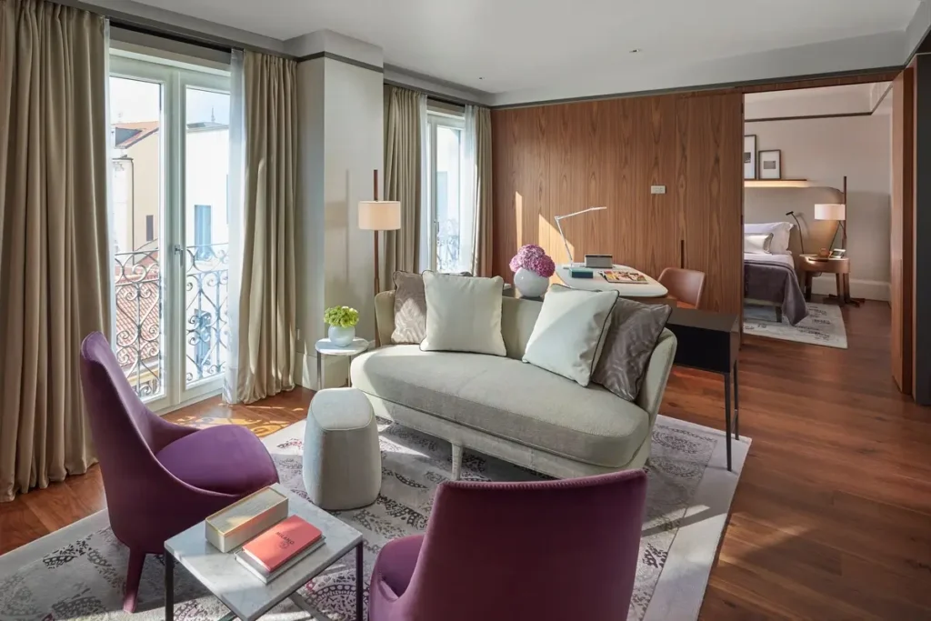 Sofa and purple armchairs in a Deluxe Suite living area, with the bedroom visible through a doorway.