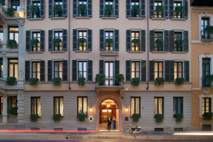 Mandarin Oriental, Milan’s pale facade with dark window shutters and an illuminated arched entrance.