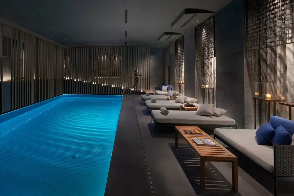 Blue indoor swimming pool beside rows of cushioned loungers and patterned screens at Mandarin Oriental, Milan.