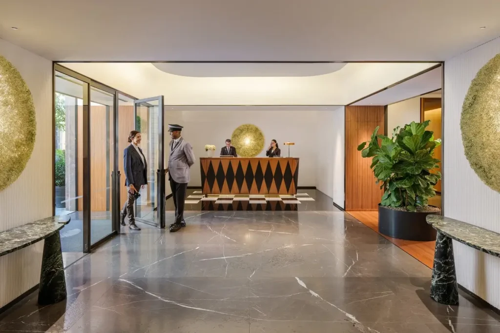 Contemporary reception desk, polished stone floor, plants, and an open doorway in the hotel lobby.