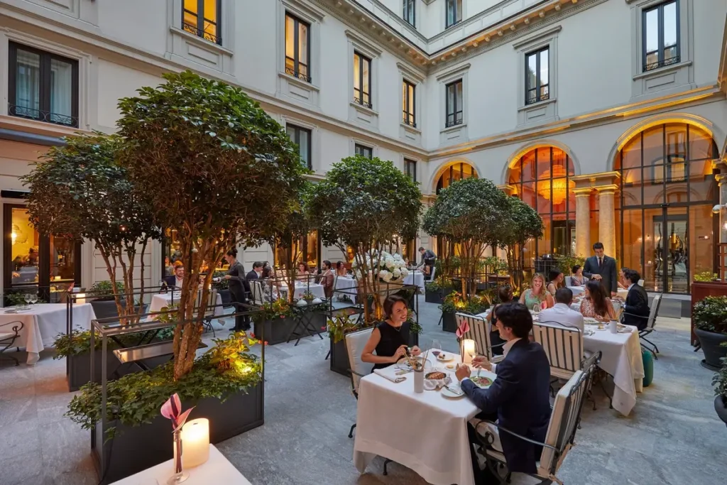 White-clothed dining tables and guests among trees in Seta’s courtyard, surrounded by historic facades.