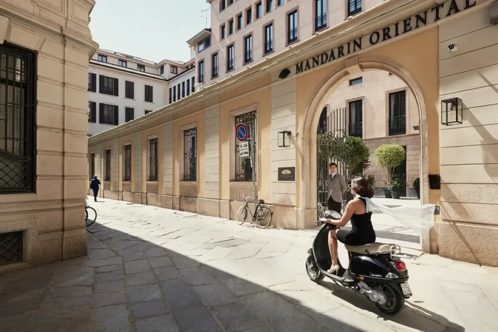 Arched Mandarin Oriental entrance beside a narrow Milan street, with a scooter passing in front.