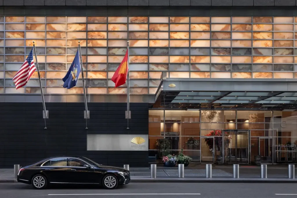 Glass entrance doors, flags, and a black car outside Mandarin Oriental, New York.