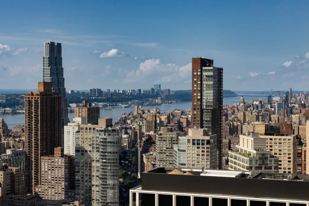 Manhattan towers with the Hudson River and distant shoreline visible beyond.