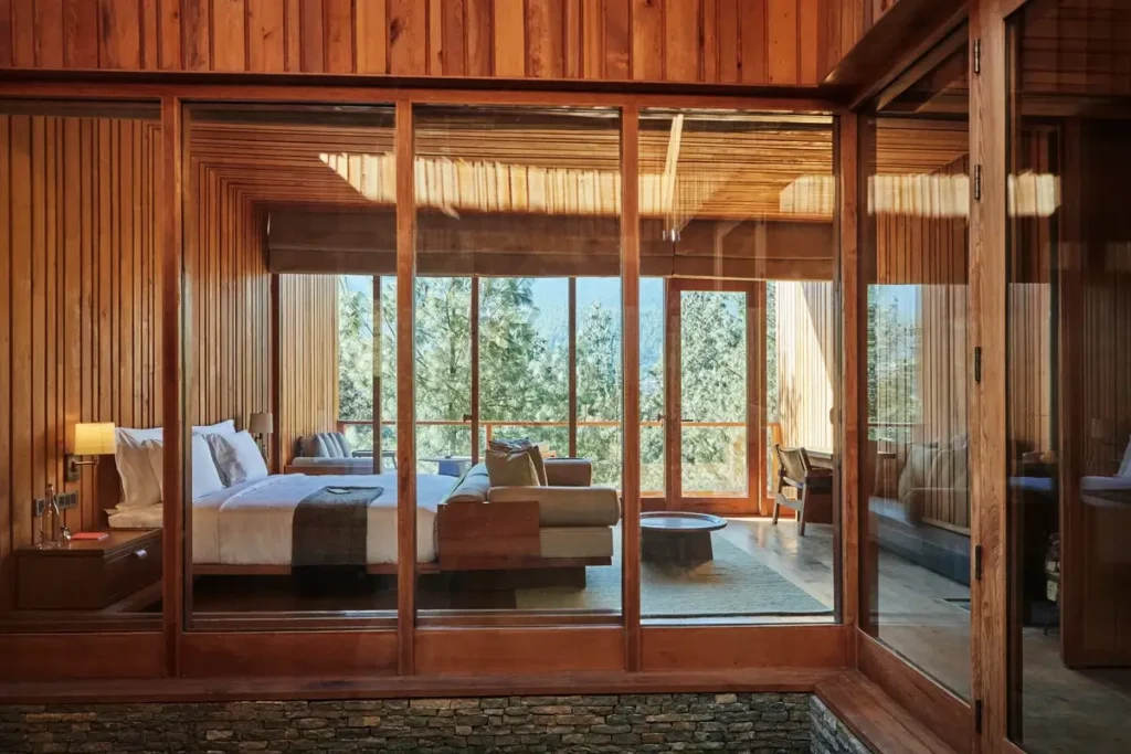 A timber-lined bedroom with a canopy bed is seen through glass walls across a small courtyard.